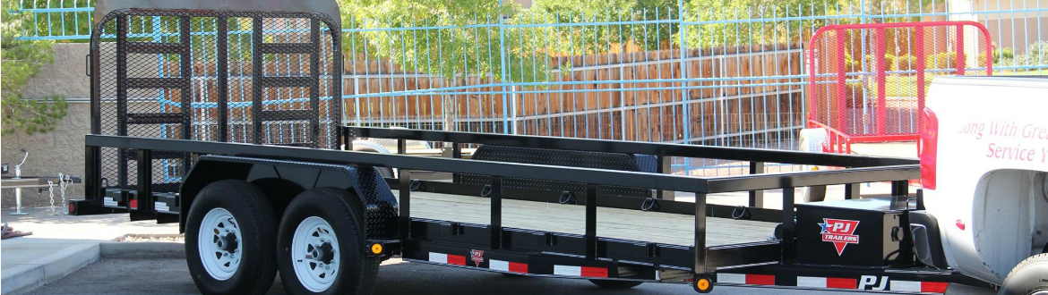 A PJ trailer attached to a white truck and sitting in a lot with other trailers.