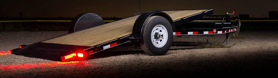 A tilt trailer angled at the ground in a gravel lot at night.